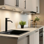 Modern kitchen with a black sink and matte black faucet, white cabinets, and under-cabinet lighting over a light countertop.